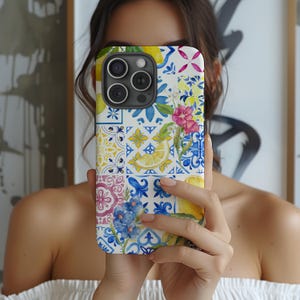 May include: A white iPhone case featuring a colourful pattern of lemons, flowers, and blue and white tiles. The case has a camera lens cutout.