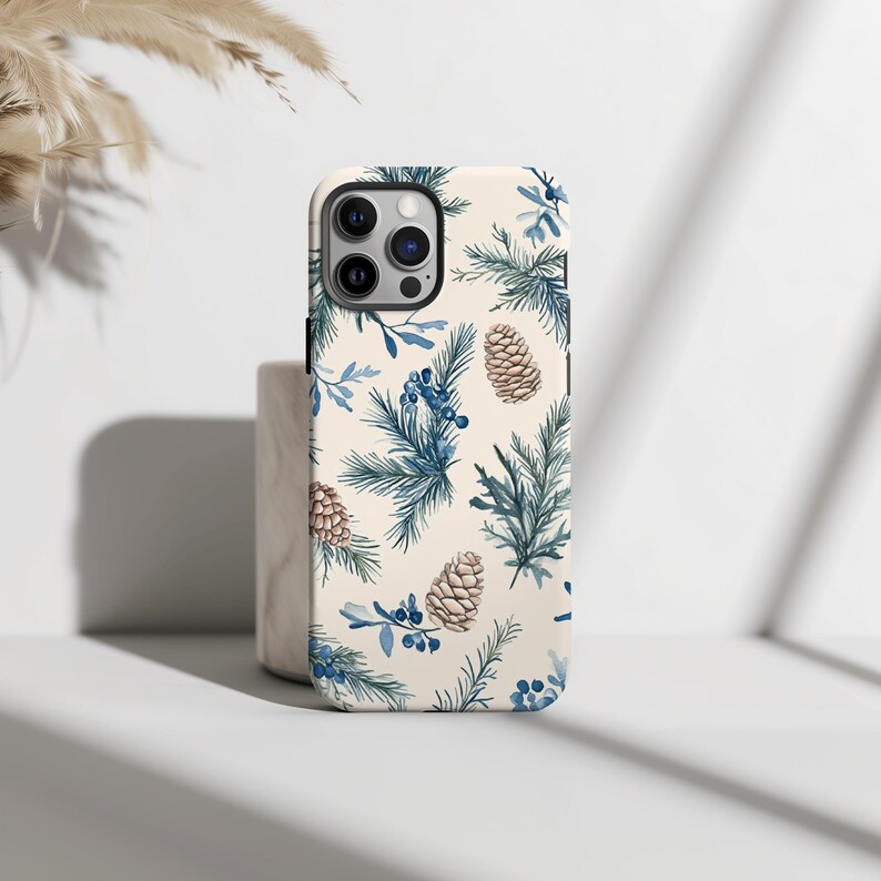 May include: A white phone case with a blue and brown pine cone and evergreen pattern.
