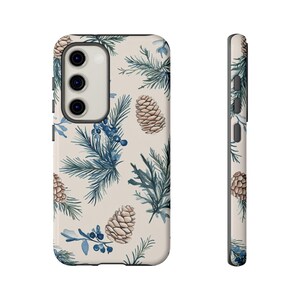 May include: A cream-colored phone case with a pattern of blue pine branches, brown pine cones, and blue berries.