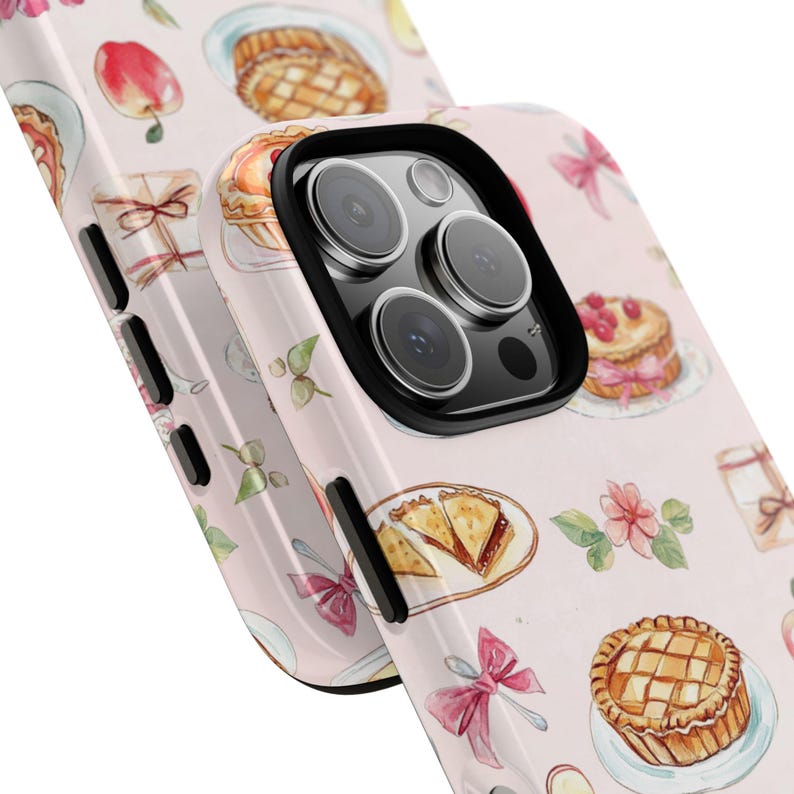 K&ouml;nnte beinhalten: Eine rosa Handyh&uuml;lle mit einem Aquarelldesign aus Torten, Geb&auml;ck und Schleifen. Die H&uuml;lle hat eine schwarze Kameraerh&ouml;hung mit drei Objektiven.