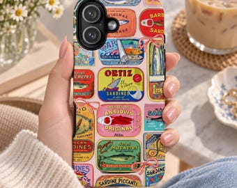Może przedstawiać: Etui na smartfona z kolorowym kolażem etykiet puszek po sardynkach i makrelach w stylu vintage. Wzór zawiera różne prostokątne i owalne grafiki z napisami takimi jak Ortiz, Ansjovis i Small Mackerel, ozdobione różowymi kokardkami.