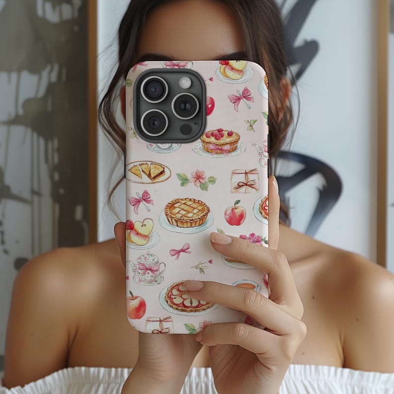 This coquette phone case features charming watercolor illustrations of pies, teacups, apples, and bows on a soft pink background. Its delicate, whimsical design exudes a vintage, feminine charm perfect for adding a touch of elegance.