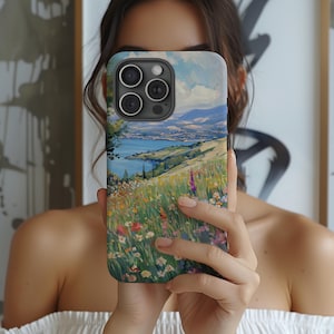May include: A phone case featuring a colourful landscape painting of a field of flowers with a body of water in the distance. The case has a camera lens cutout.