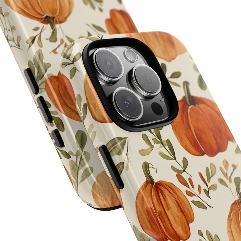 May include: A close-up of a phone case with a seasonal design. The case has a cream background with orange pumpkins and green leaves in a watercolour style. The phone's camera lenses are visible, framed by a black border.