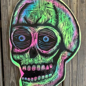 Puede incluir: Una calavera negra y blanca con un efecto de pintura iridiscente verde, rosa y azul. La calavera tiene un dise&ntilde;o detallado con l&iacute;neas y sombras.
