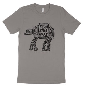 Puede incluir: Una camiseta gris jaspeada con un gráfico negro de un caminante AT-AT de Star Wars. El texto "Sean Star Wars" está impreso en el cuerpo del caminante.