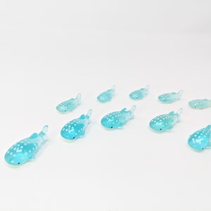 May include: A group of ten small, blue, spotted whale shark figurines. The figurines are made of plastic and are about 2 inches long.
