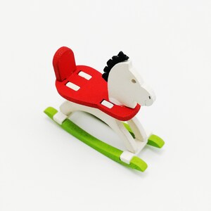 Op de afbeelding: Een wit houten schommelpaard met een rood zadel en groene wiegen. Het paard heeft een zwarte manen en staart.