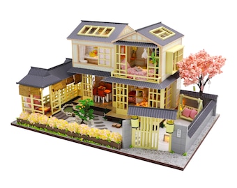 Pode incluir: Uma casa de bonecas de madeira em miniatura com um design de estilo japonês. A casa tem um telhado cinza, paredes amarelas e um pequeno jardim com uma cerejeira em flor. A casa tem uma varanda, uma sacada e uma cerca. A casa é decorada com móveis e acessórios em miniatura.