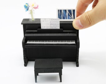 May include: A black miniature piano with a music sheet, a small stool, and a vase with colorful flowers. The piano has a white frame and a black and white keyboard.