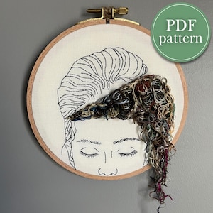 May include: Embroidered hoop art featuring a line drawing of a person's face with their hair represented by a tangle of colourful embroidery floss.