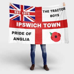 May include: A white flag with a Union Jack in the upper left corner and a red cross. Text includes "EST 1878", "IPSWICH TOWN", "PRIDE OF ANGLIA", and "THE TRACTOR BOYS". A red poppy is on the right.
