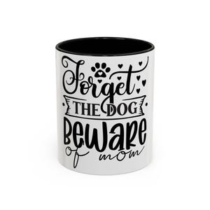 May include: White ceramic coffee mug with a black interior. The mug features the text "Forget the dog, beware of mom" in black script, along with paw prints and hearts. A fun gift for dog lovers and moms.