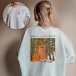 Może przedstawiać: Szara bluza z napisem "Girls Gone Mild in the Wild" i grafiką lasu z dużymi drzewami.