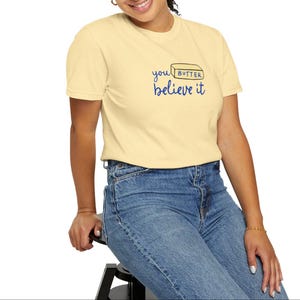 May include: A light yellow t-shirt with a blue and black graphic that says "you butter believe it" and a stick of butter illustration.