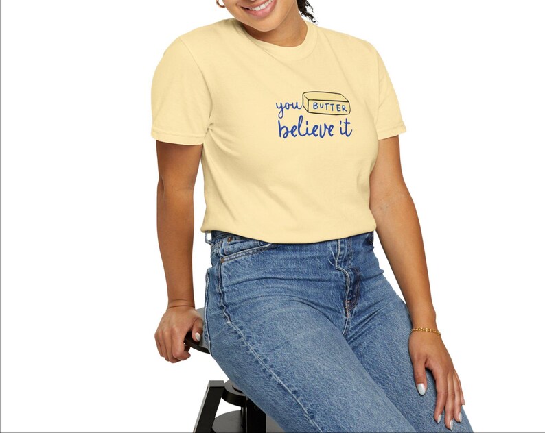 May include: A light yellow t-shirt with a blue and black graphic that says "you butter believe it" and a stick of butter illustration.