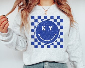 May include: A gray sweatshirt with a blue and white checkered pattern and a blue smiley face with the letters "KY" inside.