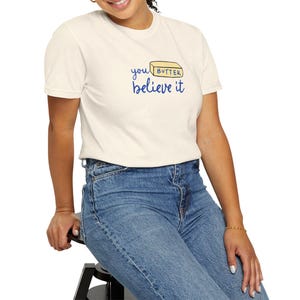 May include: A white t-shirt with a blue graphic that says "you butter believe it" and a yellow stick of butter with the word "butter" on it.