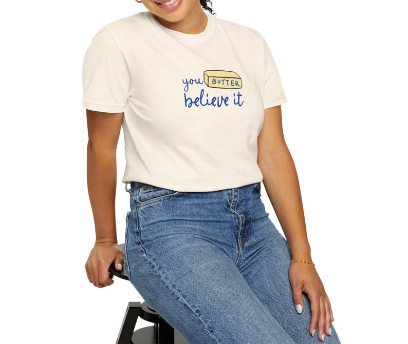 May include: A white t-shirt with a blue graphic that says "you butter believe it" and a yellow stick of butter with the word "butter" on it.