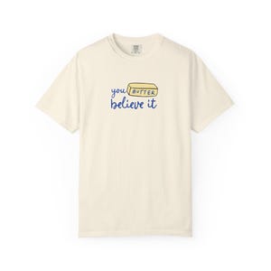 May include: A cream colored t-shirt with a blue and yellow graphic that says "you butter believe it" with a stick of butter illustration.