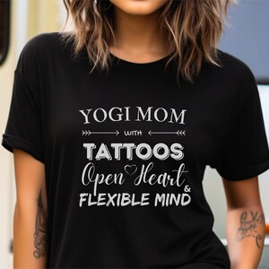 May include: Black t-shirt with white text that reads "Yogi Mom with Tattoos Open Heart & Flexible Mind".