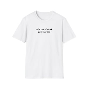 May include: White t-shirt with the text "ask me about my turtle" in black, centered on the chest. The shirt has short sleeves and a crew neck. The fabric appears to be a soft cotton blend.
