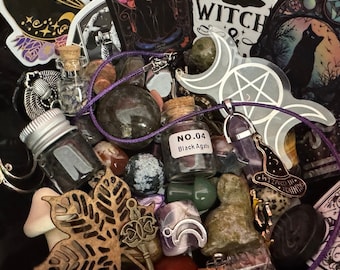 May include: A black bowl filled with a variety of witchy items, including crystals, a necklace with a pentagram pendant, small glass bottles, and stickers with witchy themes. The stickers feature images of cats, moons, and the words "Witch" and "Wicca".