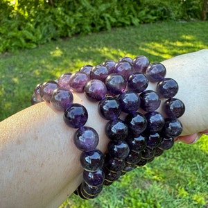 May include: A stack of amethyst gemstone bracelets with round beads. The bracelets are purple and have a shiny finish.