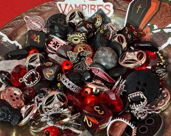 Peut inclure: Une collection de bijoux et d'accessoires sur le thème gothique, comprenant des bagues, des dés, des boutons et des breloques. Les articles sont dans les tons noir, rouge et argent, avec des motifs de vampires et de cercueils. Le mot "VAMPIRES" est visible.