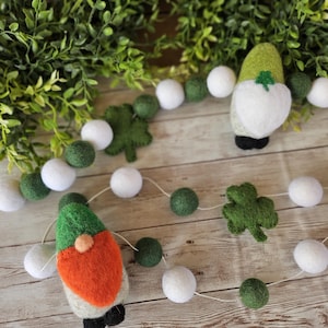 Op de afbeelding: Een St. Patrick's Day slinger met vilten kabouters met oranje baarden en groene hoeden, witte vilten ballen, groene vilten ballen en vilten klavers. De slinger is geregen op een wit touwtje.