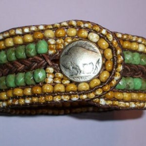May include: A brown leather bracelet with a silver buffalo nickel coin as a clasp. The bracelet is decorated with green and brown beads.