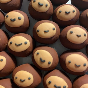 May include: A collection of brown and beige painted round ornaments with smiling faces. Each ornament has a different facial expression.