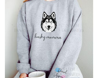 Op de afbeelding: Grijs sweatshirt met een zwart-witte husky-hond afbeelding en de tekst "husky momma". De mouwen hebben blauwe en roze poot afdrukken met de tekst "Diesel Aspen".