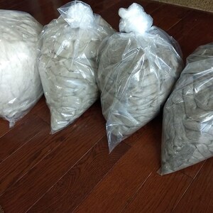May include: Four plastic bags filled with different shades of gray wool fiber. The bags are arranged in a row on a wooden floor.