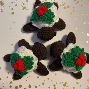Op de afbeelding: Drie gehaakte schildpad ornamenten met bruine schalen en witte lichamen versierd met groene hulst en rode bessen.
