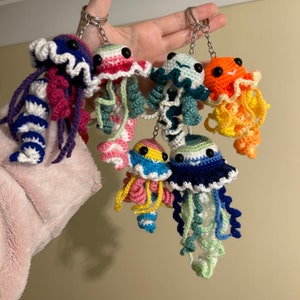 May include: A set of crocheted jellyfish keyrings in various colours, including pink, blue, green, yellow, and orange. Each keyring features a detailed crocheted jellyfish with a curled tentacle.