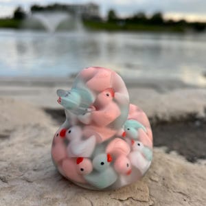 May include: A clear glass duck figurine filled with smaller duck figurines in pink, blue, and white.