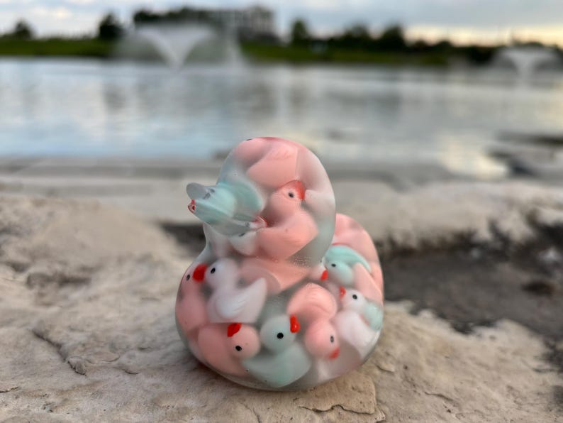 May include: A clear glass duck figurine filled with smaller duck figurines in pink, blue, and white.