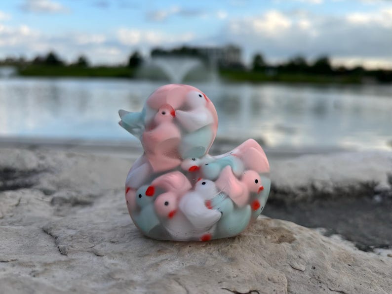 May include: A clear plastic duck figurine filled with smaller duck figurines in pink, white, and blue.