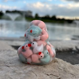 May include: A pink and blue rubber duck with multiple smaller ducks inside. The ducks are all different colors and have red beaks.