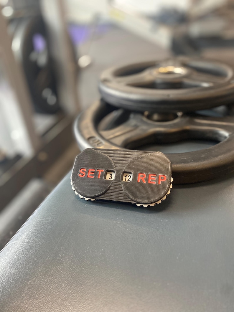 May include: Black and red workout counter with the words "SET" and "REP" on either side. The counter displays "3" for sets and "12" for reps.