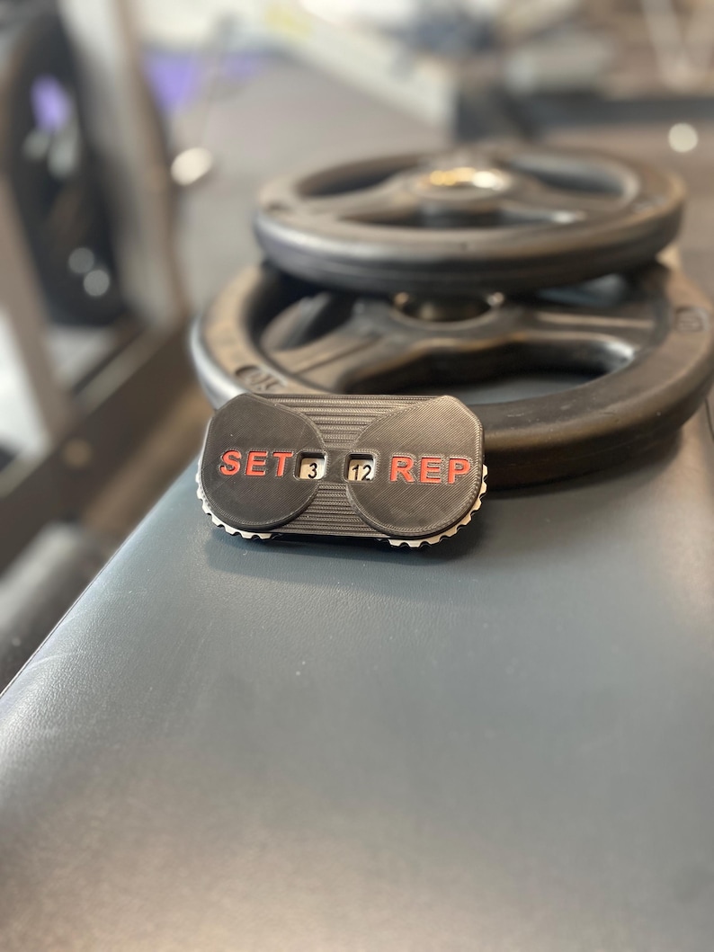 May include: A black and red workout counter with the words "SET" and "REP" on either side of a digital display showing "3" and "12".