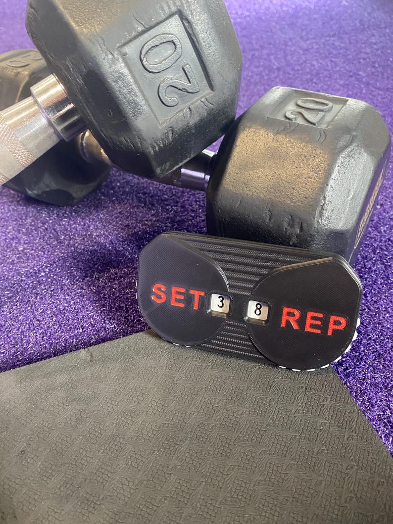 May include: Two black 20 pound dumbbells with a black and red counter that reads "SET 3 8 REP" on a purple mat.