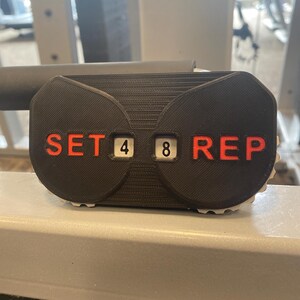 May include: Black and gray counter with a black and red counter for sets and reps. The counter displays "SET 4 8 REP".
