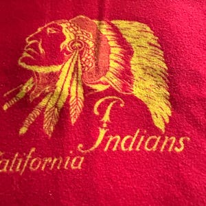 May include: Red fleece blanket with a gold embroidered image of an American Indian wearing a headdress. The text "California Indians" is embroidered below the image.