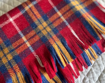 May include: Red, blue, yellow, and white plaid throw blanket with fringe. The blanket is folded in half and has a soft, fuzzy texture.