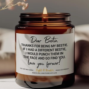 May include: A brown glass candle jar with a white label that reads "Dear Bestie, THANKS FOR BEING MY BESTIE. IF I HAD A DIFFERENT BESTIE, I WOULD PUNCH THEM IN THE FACE AND GO FIND YOU. love you forever!"  The candle is lit and the label also includes the text "9 OZ SOY WAX CANDLE Light-It-Wonder VEGAN ECO FRIENDLY MADE IN USA HAND POURED WITH LOVE."