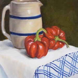 May include: A white pitcher with blue stripes sits on a white tablecloth with a blue and white checkered border. Two red peppers are next to the pitcher.