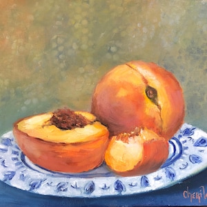 Puede incluir: Una pintura de bodegón con tres melocotones en un plato con un patrón azul y blanco. Un melocotón está cortado por la mitad, revelando la pulpa y el hueso. Los melocotones están sobre un fondo azul.