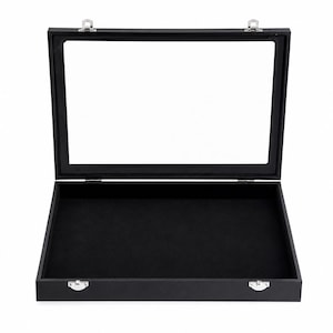 May include: A black display case, open to reveal a clear glass top and a black velvet interior. The case features silver-coloured metal hinges and a clasp. The rectangular case is designed for displaying collectibles.